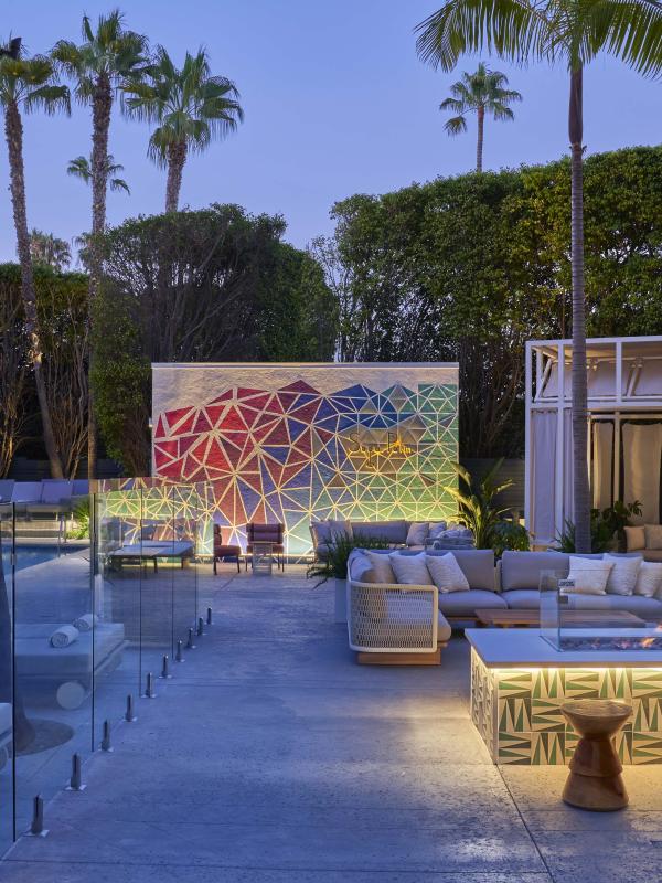 An outdoor gathering space with couches around a fire pit and cabanas surrounding a pool