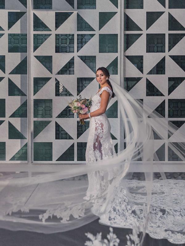 A bride poses with her bouquet next to a concrete mosaic wall