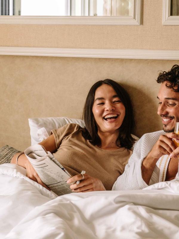 A couple laying in bed with the paper and a mimosa