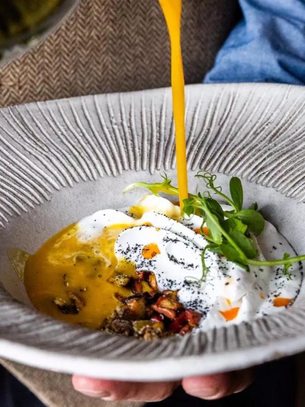 A server pour vinaigrette on an egg and greens dish
