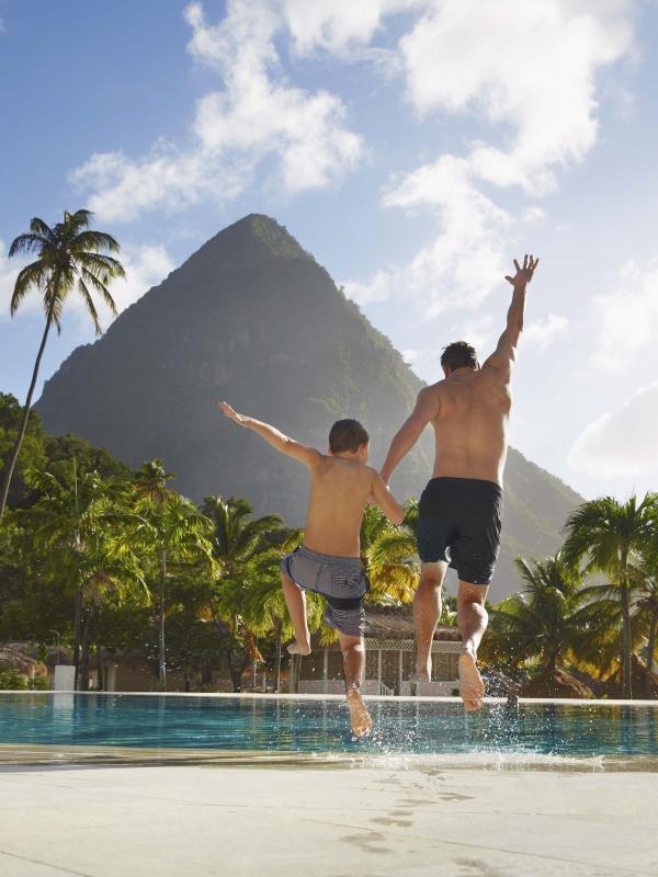 A father and son jumping into the pool at Viceroy Sugar Beach with beautiful mountains ion the foreground