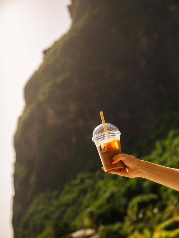 A hand holding up an iced coffee to the sun with the beach in the background