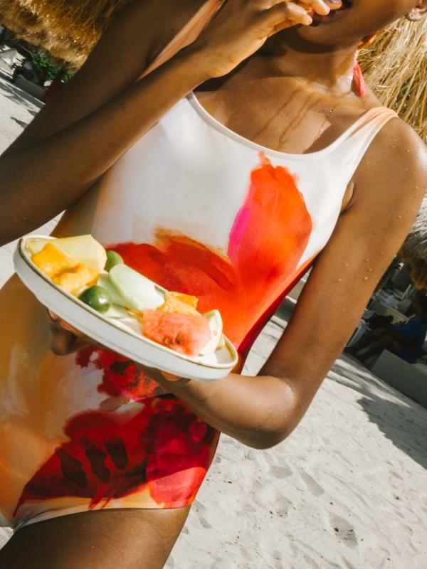 A woman in a bathing suit eats fresh fruit on the beach.