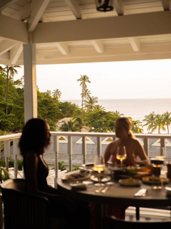 Two women talking while dining on a patio with beach front in the background.