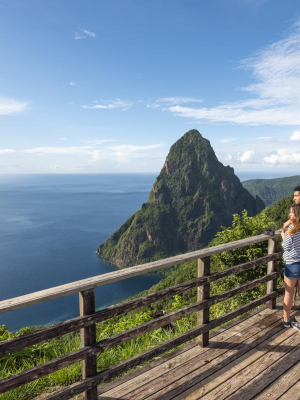 A couple looks out at the ocean and a tropical mountain from a viewing platform atop a ridge
