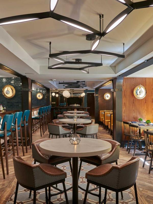 The dining room of Dovetail restaurant at Viceroy Washington DC, with a row of yellow booths adjacent to a long bar seating area