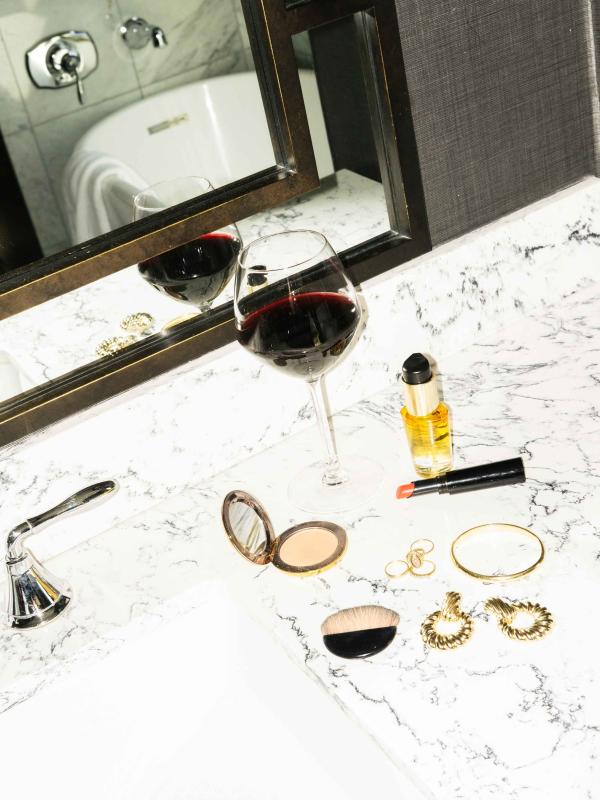 A glass of red wine and make up laid out on a white marble countertop