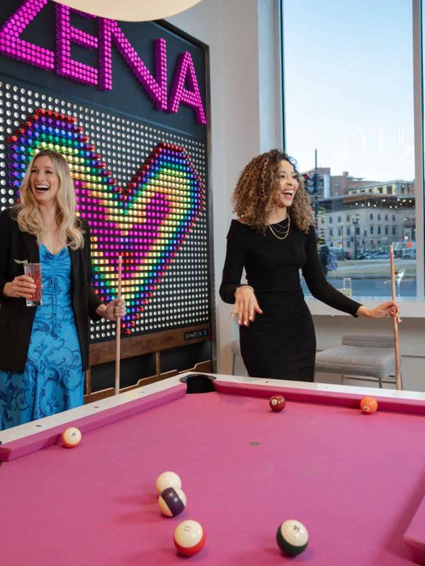 Two women shoot pool on a pink pool table at Hotel Zena's Figleaf restaurant