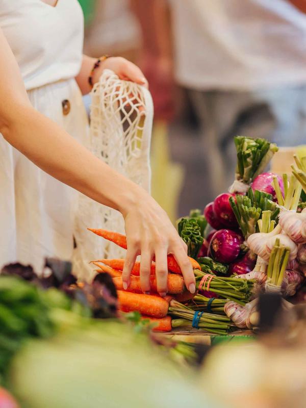 people reach for vegetables laid out on a table at market