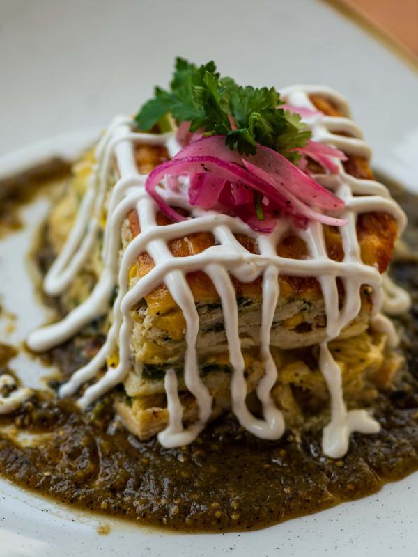 A tarte topped with pickled onions and cilantro, drizzled with crema and served on a sauce base