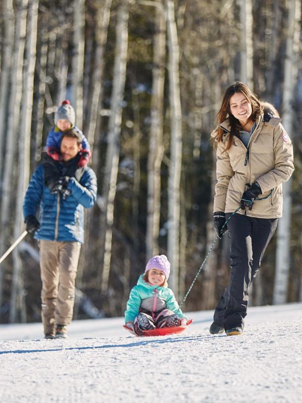 A family walks their dog in the woods at Snowmass, while pulling a child on a sled