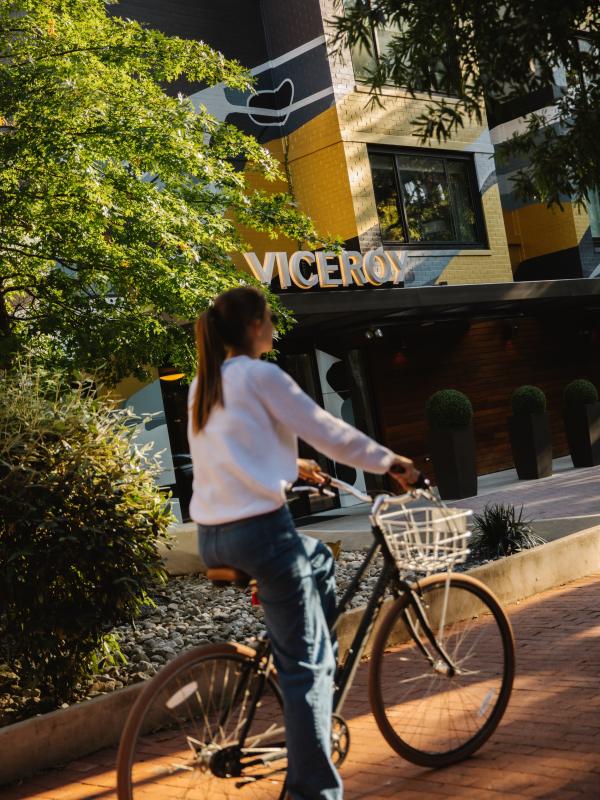 woman in white sweater rides bike in front of Viceroy