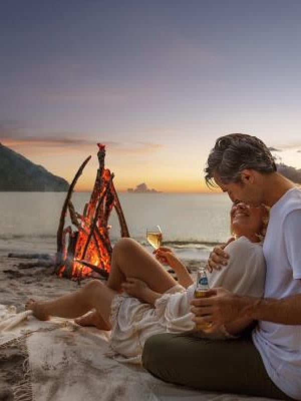 Un couple qui se fait des câlins sur la plage, près d'un feu