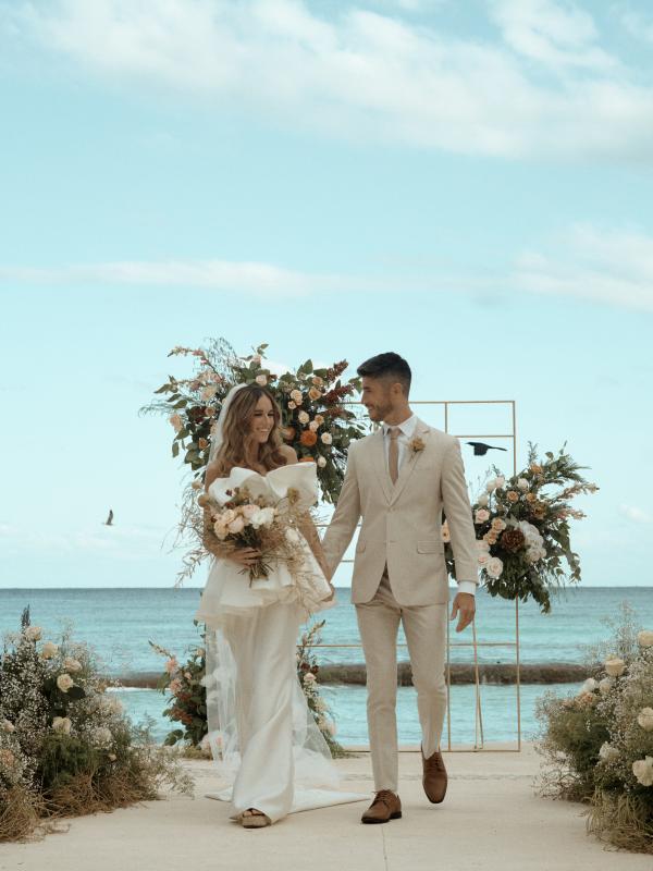 A newly married couple walk hand in hand back down the aisle, smiling at one another. 