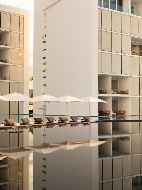 A mirror-like pool with the hotel and lounge chairs in the background.
