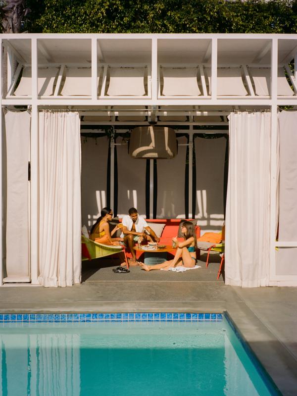 Three friends sit in a cabana, sipping drinks and talking.