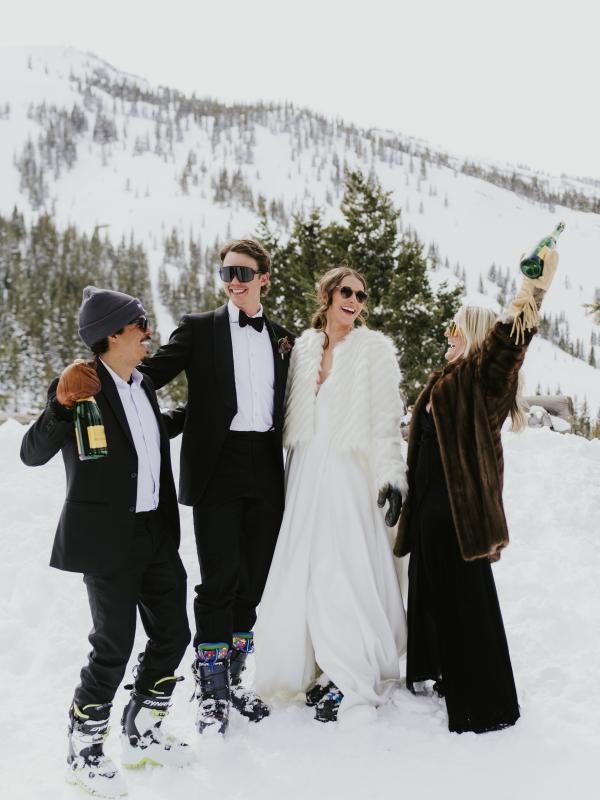 The bride and groom and their friends celebrating in the snow with champagne 