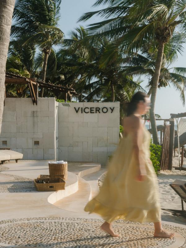 Une femme vêtue d'une robe jaune passe devant un mur sur lequel est accrochée une pancarte indiquant «VICEROY » dans une station balnéaire tropicale.