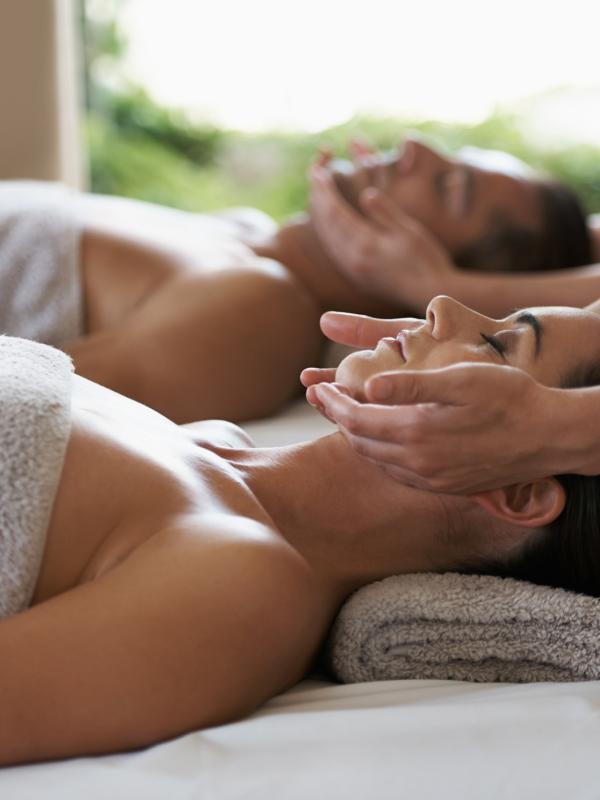 Un hombre y una mujer tumbados en una camilla de masaje mientras les dan un tratamiento facial en un spa