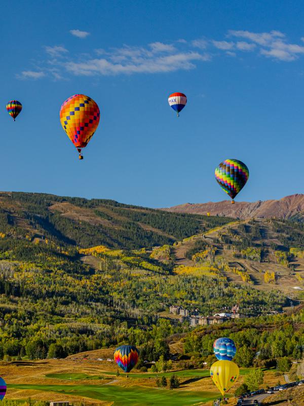 Une douzaine de montgolfières survolent la ville de Snowmass, avec les montagnes verdoyantes en arrière-plan