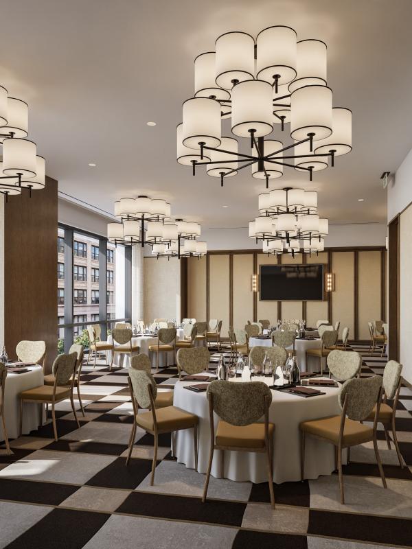 A spacious dining room has round tables set with white cloths and glassware, upholstered chairs, large chandeliers, and tall windows overlooking city buildings.