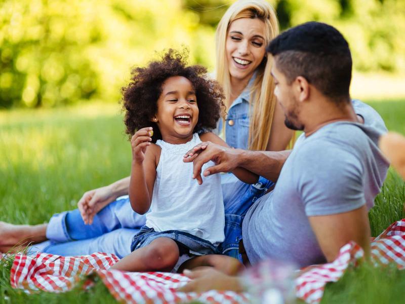 family sits on red checkered blanket in a park