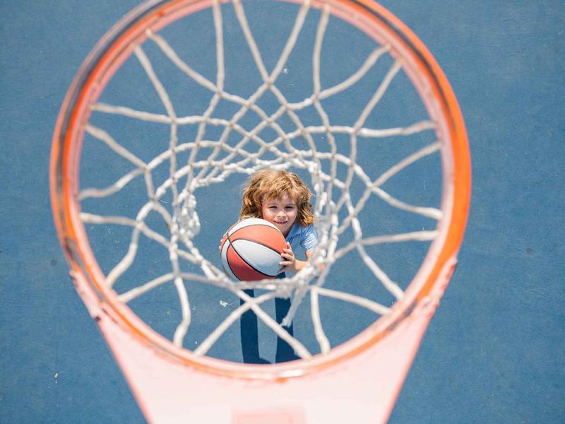 child holding a basketball looks up through a basketball net