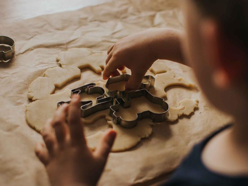 kid sitting at a table uses cookie cutter to cut dough into shapes