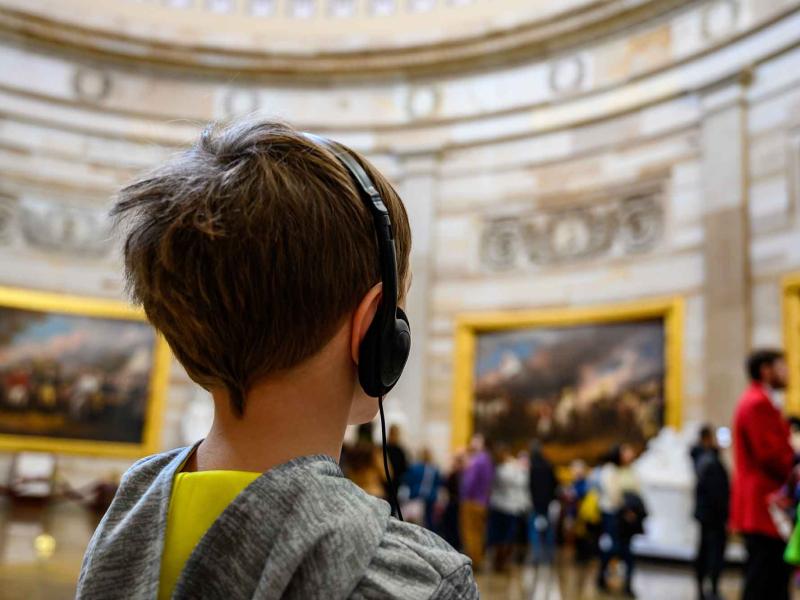child with brown hair stands in a museum wearing headphones