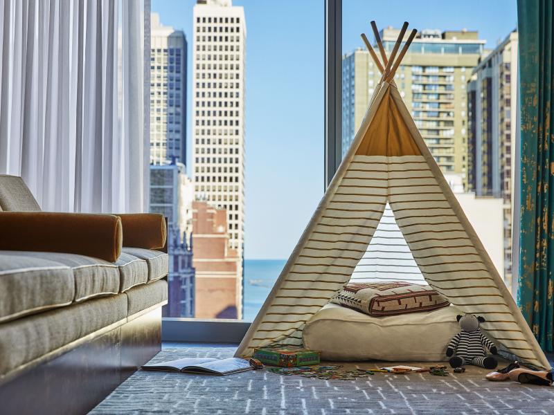 A triangular teepee-style children's pop-tent set up in a hotel room looking out on the Chicago skyline