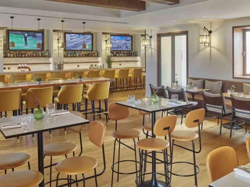 The Casa e Fora dining room at Ombria Algarve, with high four-top tables and a long bar section with wall-mounted televisions