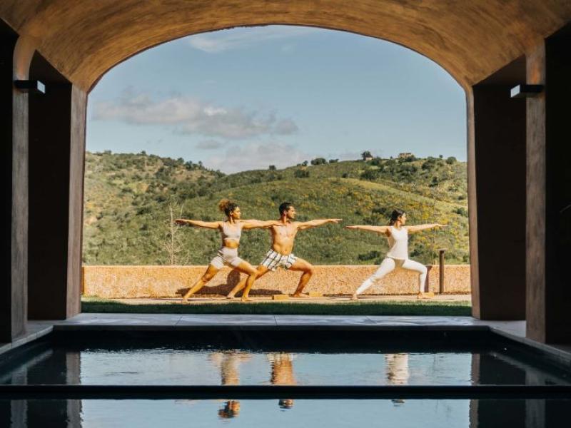 Three people doing yoga in a spa courtyard at Viceroy Ombria Algarve, with hills in the background