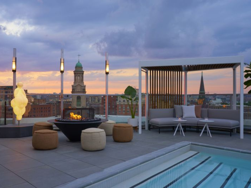 A rooftop patio with a bankette couch, ottomans and torch lighting