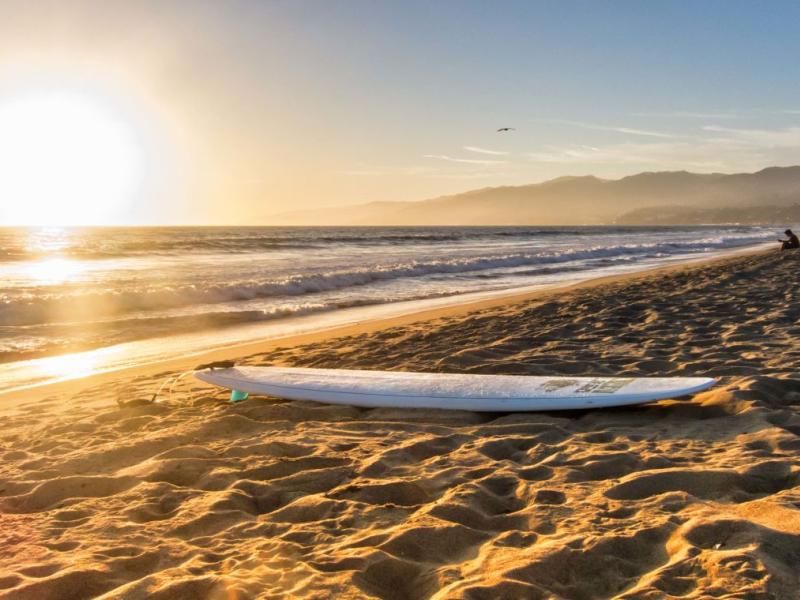 A surfboard lying on a Santa Monica beach at sunset