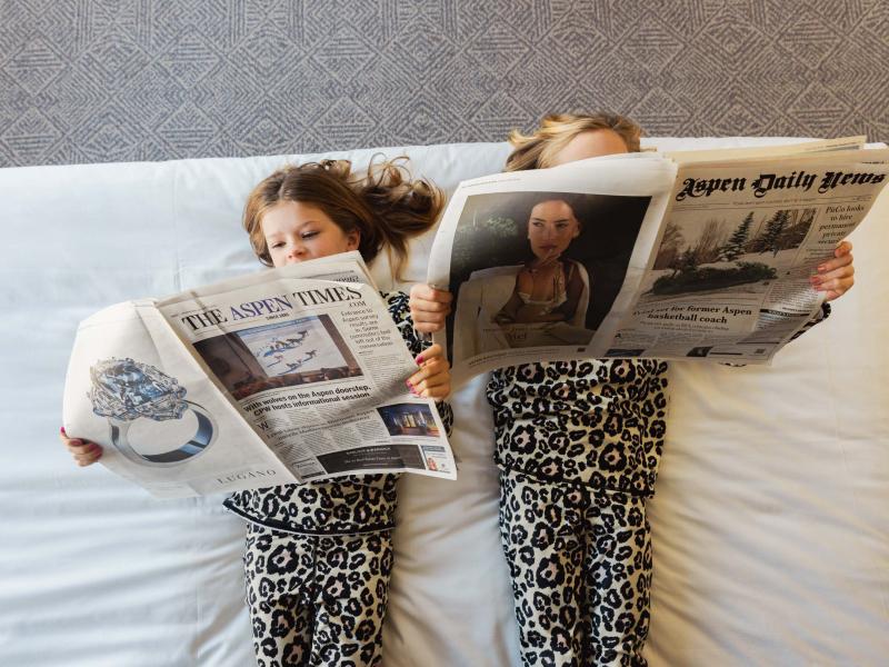 Two kids reading newspapers on a bed
