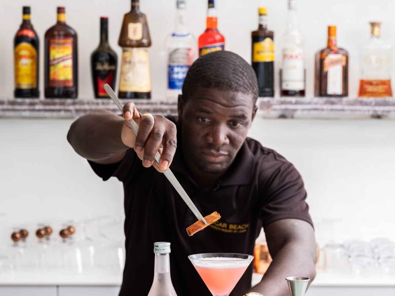 A bartender places the finishing garnish on a pink cocktail at The Cane Bar