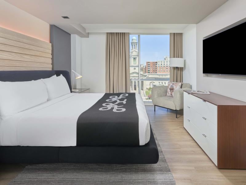 A king bed, dresser, TV, chair, and balcony in a room at Viceroy Zena Washington DC