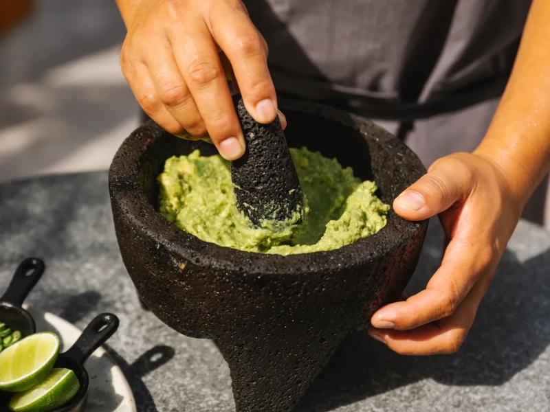 A man makes guacamole in a stone molcajete