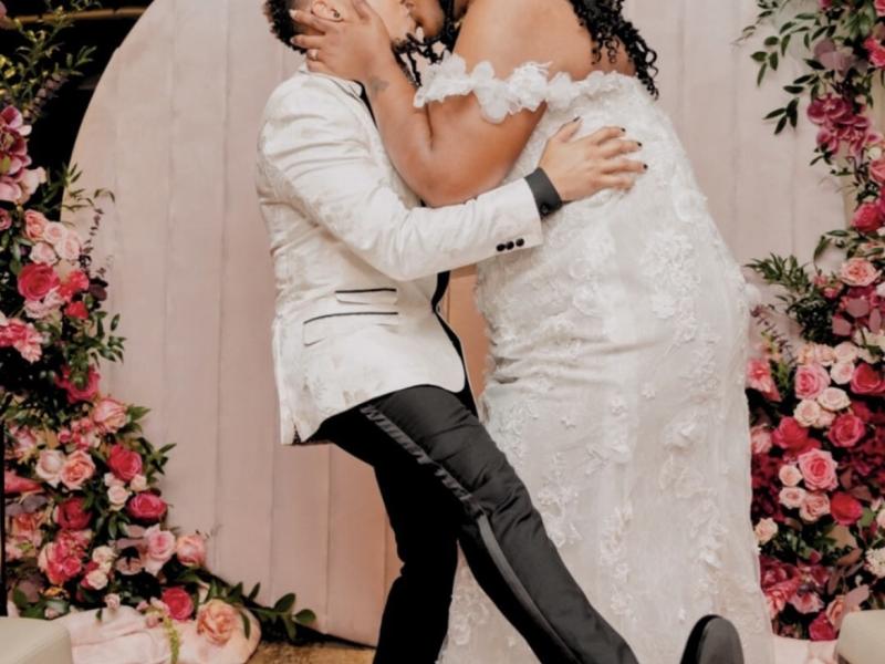 A Bride and Groom kissing under a floral arch