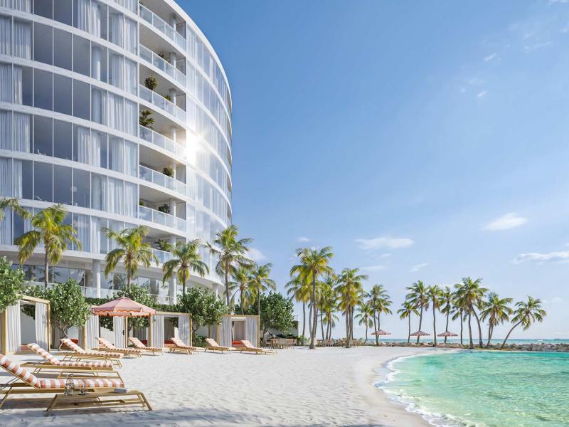 Un bâtiment moderne aux lignes courbes surplombe une plage de sable blanc immaculée, agrémentée de transats, de cabanes, de palmiers et d'une eau turquoise cristalline.