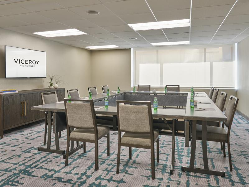 Modern hotel conference room with U-shaped tables, cushioned chairs, bottled water, and a wall-mounted Viceroy display.