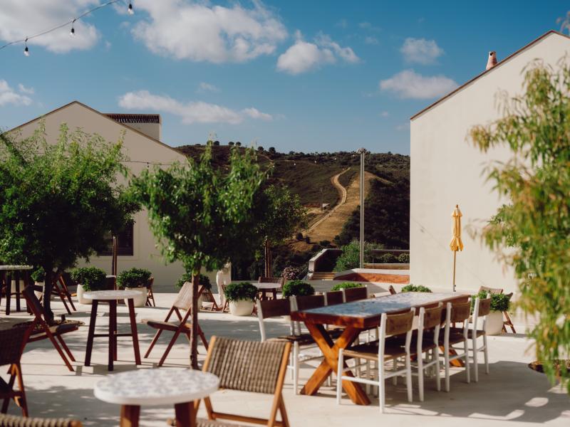 Um terraço ao ar livre com mesas de jantar e a paisagem rural do Algarve como pano de fundo